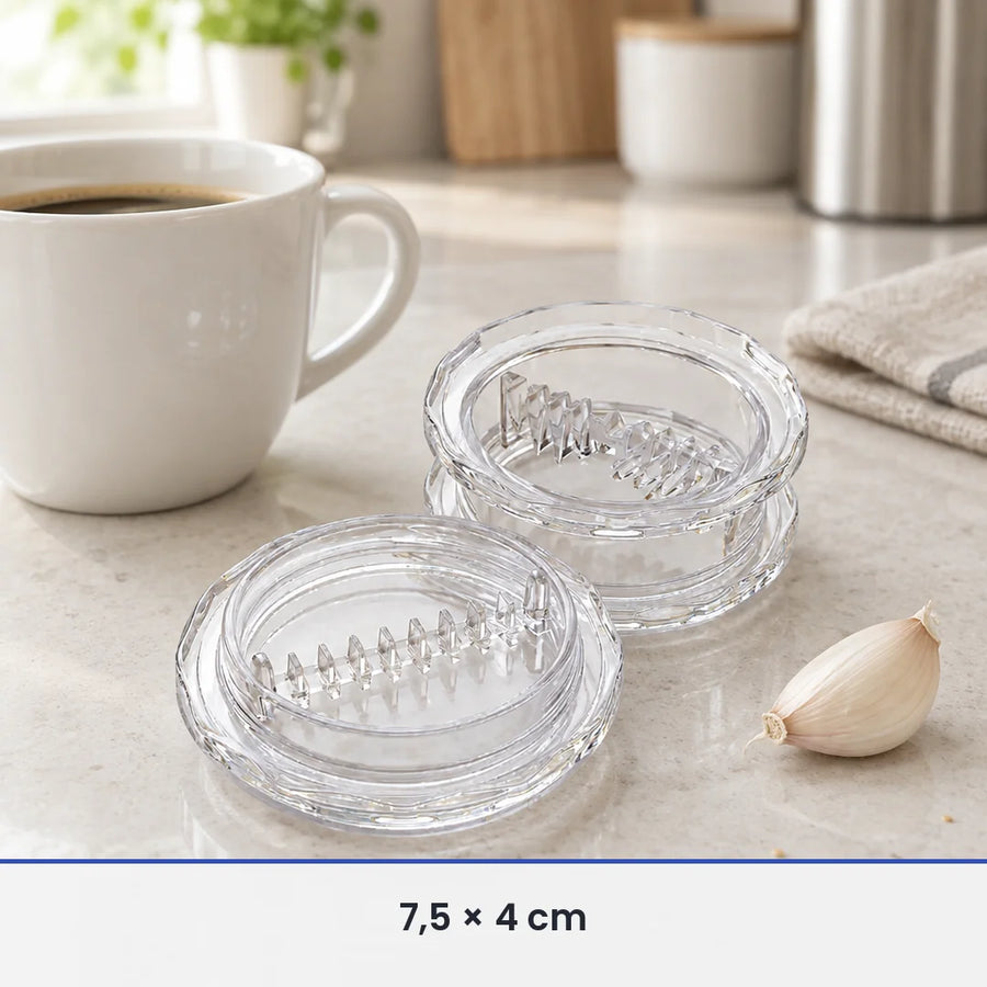 Hachoir à ail transparent de 7,5 cm de diamètre ouvert à côté d'une tasse à café et d'une gousse d'ail, pour l'échelle