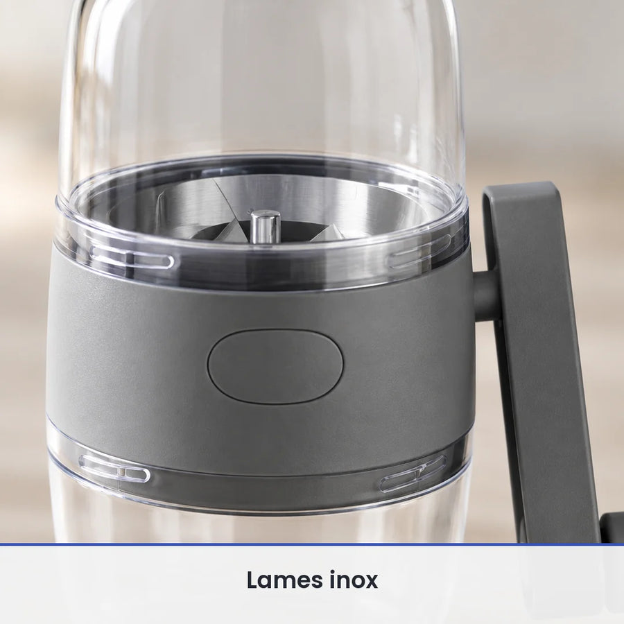 Gros plan sur le corps gris du hachoir à noix et les éléments de coupe inox visibles sous le réservoir transparent