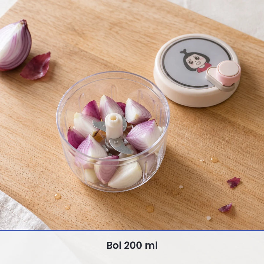 Bol transparent de 200 ml du hachoir rotatif rempli de quartiers d'oignon, couvercle beige rosé posé à côté