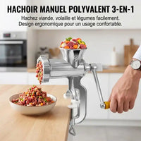 Hachoir Manuel Polyvalent 3-en-1 : Hachoir manuel en fonte chromée avec manche en bois jaune, fixé sur un plan de travail en bois. Un homme hache de la viande et des légumes frais (bœuf, carottes, oignons) qui tombent dans un bol décoré. Le texte superposé indique « HACHOIR MANUEL POLYVALENT 3-EN-1 »