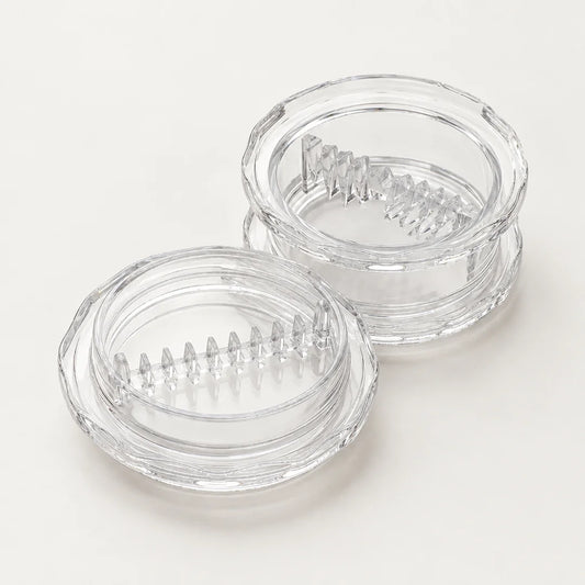 Hachoir à ail à torsion en plastique transparent, ses deux parties ouvertes côte à côte avec leurs dents de coupe en relief
