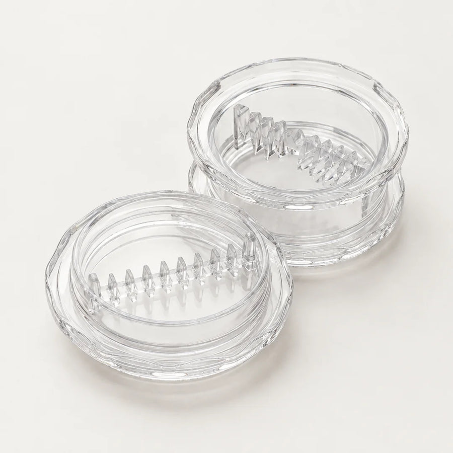 Hachoir à ail à torsion en plastique transparent, ses deux parties ouvertes côte à côte avec leurs dents de coupe en relief