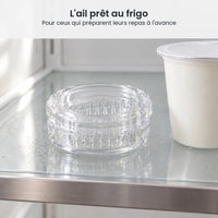 Hachoir à ail transparent fermé, rangé sur une étagère en verre de réfrigérateur à côté d'un pot de yaourt