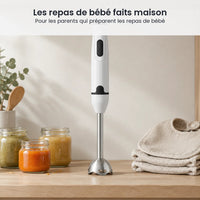 Mixeur plongeant blanc et noir rangé debout sur une étagère de cuisine claire, à côté de petits pots et de bavoirs pliés