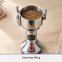 Cuve inox ouverte du moulin électrique vertical 150 g remplie de graines de coriandre, posée sur un plan de travail