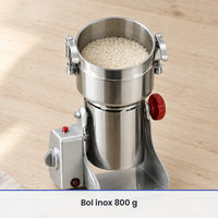 Cuve inox ouverte du moulin électrique 800 g remplie aux deux tiers de grains de riz, sur un plan de travail en bois clair