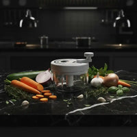 Hachoir manuel 200ml gris sur marbre noir entouré de légumes frais colorés — carottes, courgettes, oignons, ail et herbes vertes — éclairage cinématographique dramatique