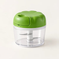 Hachoir manuel à ficelle compact avec couvercle vert pomme en forme de fleur et bol transparent, sur fond blanc cassé