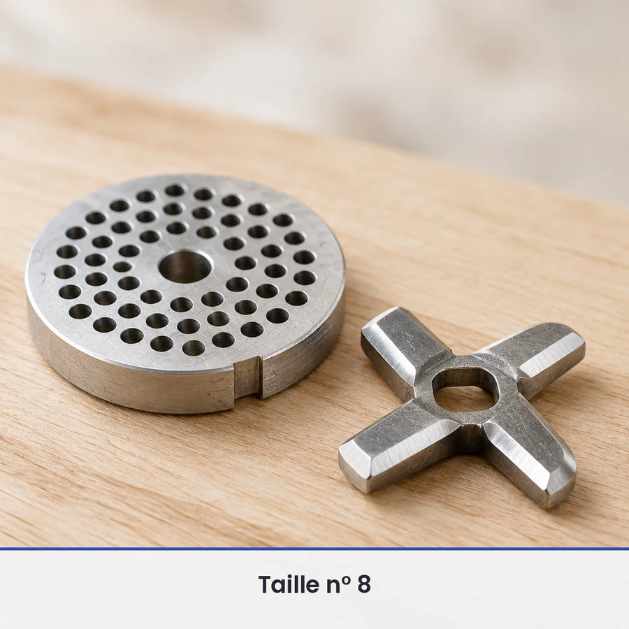 Gros plan sur la grille perforée et le couteau en croix du hachoir manuel en fonte taille 8, posés sur du bois