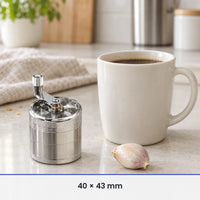 Petit moulin à épices en métal argenté de 40 × 43 mm à côté d'une tasse à café et d'une gousse d'ail, pour l'échelle