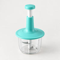 Hachoir à presse verticale avec poussoir à tige blanche, bouton et collerette turquoise, bol transparent, sur fond clair