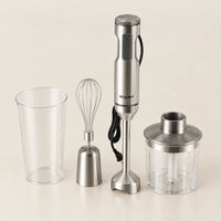 Mixeur plongeant ROUNY 4 en 1 de 1000 W en inox brossé avec gobelet gradué, fouet et bol hachoir, sur fond blanc cassé