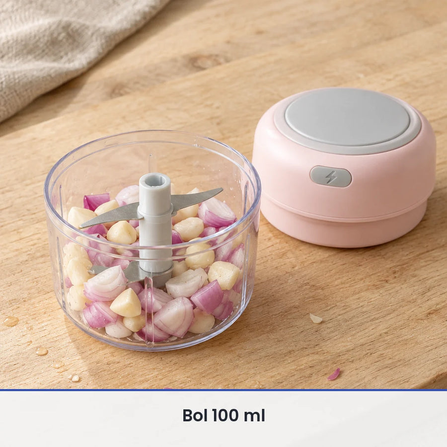 Bol transparent de 100 ml du mini hachoir électrique rose rempli d'ail et d'échalote, couvercle-moteur rose posé à côté