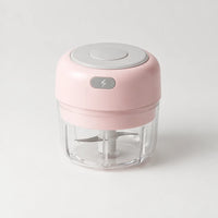 Mini hachoir électrique rose poudré 30 W avec bol transparent de 100 ml et bouton gris à éclair, sur fond blanc cassé