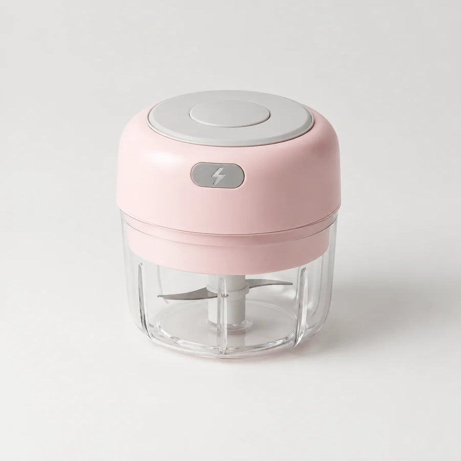 Mini hachoir électrique rose poudré 30 W avec bol transparent de 100 ml et bouton gris à éclair, sur fond blanc cassé