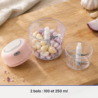 Bol de 250 ml du mini hachoir rose rempli d'ail et d'échalote, couvercle-moteur rose et bol de 100 ml posés à côté