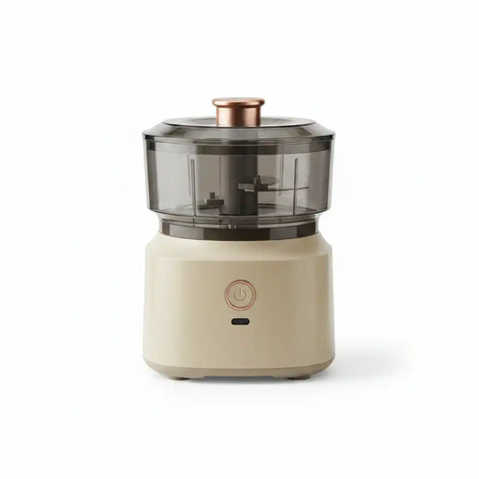 Mini hachoir électrique compact beige avec bol transparent et bouton poussoir cuivré, sur fond blanc